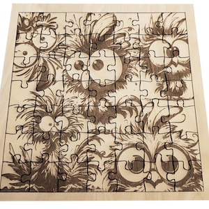 Puede incluir: Un rompecabezas de madera con un diseño caprichoso de búhos de dibujos animados. Las piezas del rompecabezas están cortadas con láser, mostrando la detallada ilustración de las caras y plumas de los búhos. El color general es marrón claro.