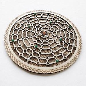 Könnte beinhalten: Ein rundes Holzbrettspiel mit einem Netzwerk aus miteinander verbundenen Kreisen und Linien. Das Brett hat eine hellbraune Farbe mit einem detaillierten eingravierten Design. Kleine grüne, silberne und kupferfarbene Murmeln sind über das Brett verstreut.