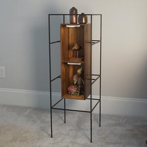 May include: A tall, black metal and wood display shelf. The wooden section has three shelves with decorative items, including small brown vases and a Buddha statue. The metal frame has a geometric design.