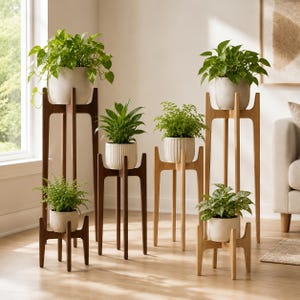 May include: A collection of six wooden plant stands in varying heights, featuring dark and light wood finishes. Each stand holds a potted green plant in a neutral-colored ceramic pot, creating a tiered display of indoor greenery.