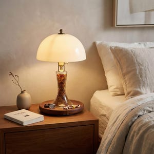 Bone china bedside lamp glowing warmly on a wooden nightstand, with a Huali wood base, recessed tray, jewelry, book, and soft bedroom setting.