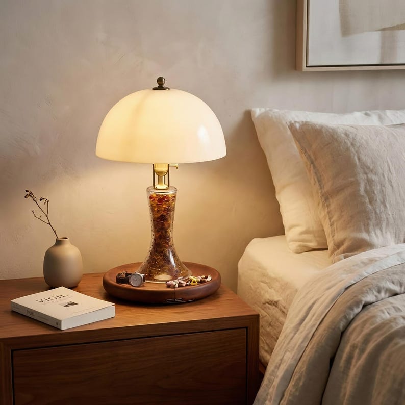 Bone china bedside lamp glowing warmly on a wooden nightstand, with a Huali wood base, recessed tray, jewelry, book, and soft bedroom setting.