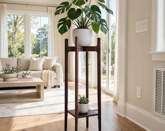 May include: A tall, dark wood plant stand with four slender legs and two tiers. A large Monstera plant in a white pot sits on the top tier, while a smaller succulent in a white pot rests on the lower square shelf.