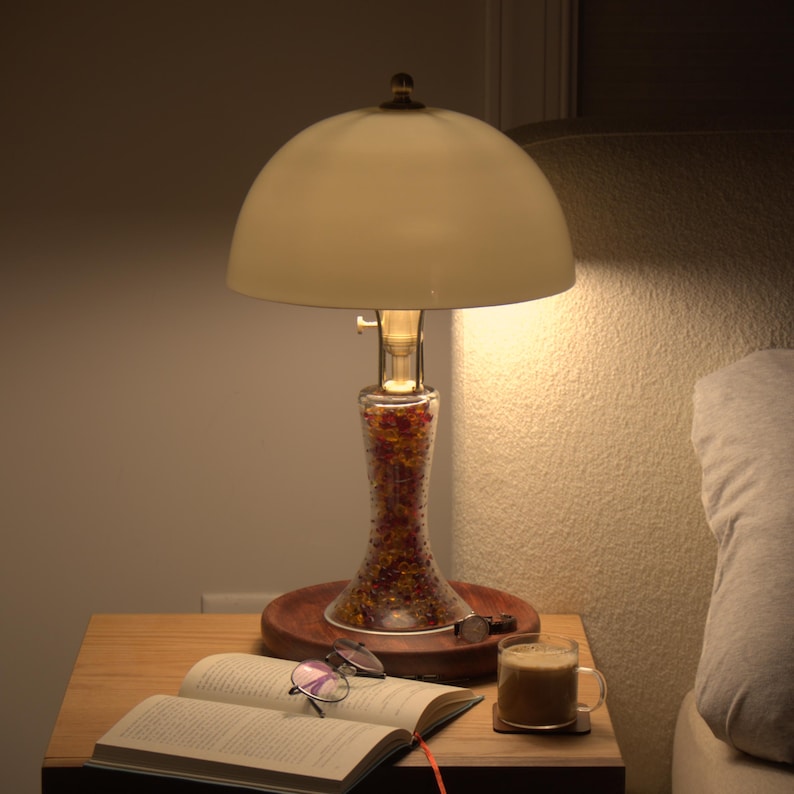 Bone china bedside lamp glowing warmly on a nightstand beside an open book, glasses, coffee, and a pillow for soft evening light.

中文意思：