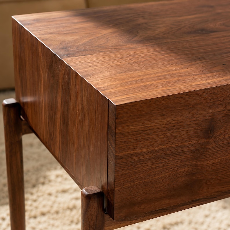 Puede incluir: Una mesa auxiliar rectangular hecha de madera de color marr&oacute;n oscuro con un patr&oacute;n de veta visible. La mesa presenta una superficie superior plana y un panel frontal liso, sostenida por patas de madera redondeadas que se extienden.