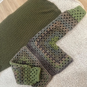 May include: A long-sleeved cardigan made of crocheted granny squares in shades of olive green, dark brown, and grey. The garment features a front opening and ribbed cuffs. Beside it lies a solid olive green knitted sweater with a ribbed texture.