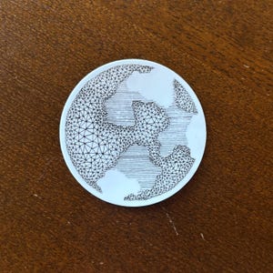 May include: A black and white line drawing of a globe with a geometric pattern. The globe is drawn in a circular shape and is on a brown wooden surface.