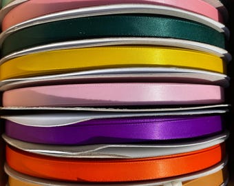 May include: A stack of spools filled with colorful satin ribbon. The ribbons are in various colors, including teal, pink, green, yellow, purple, orange, and red. The ribbon is neatly wound on cardboard spools, ready for crafting or gift wrapping.