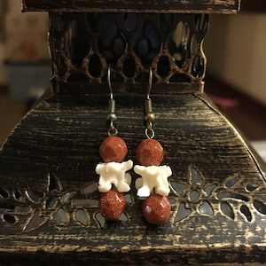 May include: A pair of earrings with red and white beads. The red beads are faceted and the white beads are shaped like vertebrae. The earrings are hanging from silver hooks.
