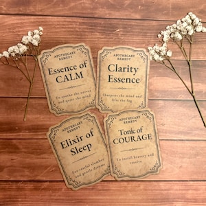 May include: Four rectangular paper labels with decorative borders and vintage-style text. The labels read Apothecary Remedy Essence of CALM, Clarity Essence, Elixir of Sleep, and Tonic of COURAGE, accompanied by two sprigs of dried white flowers.
