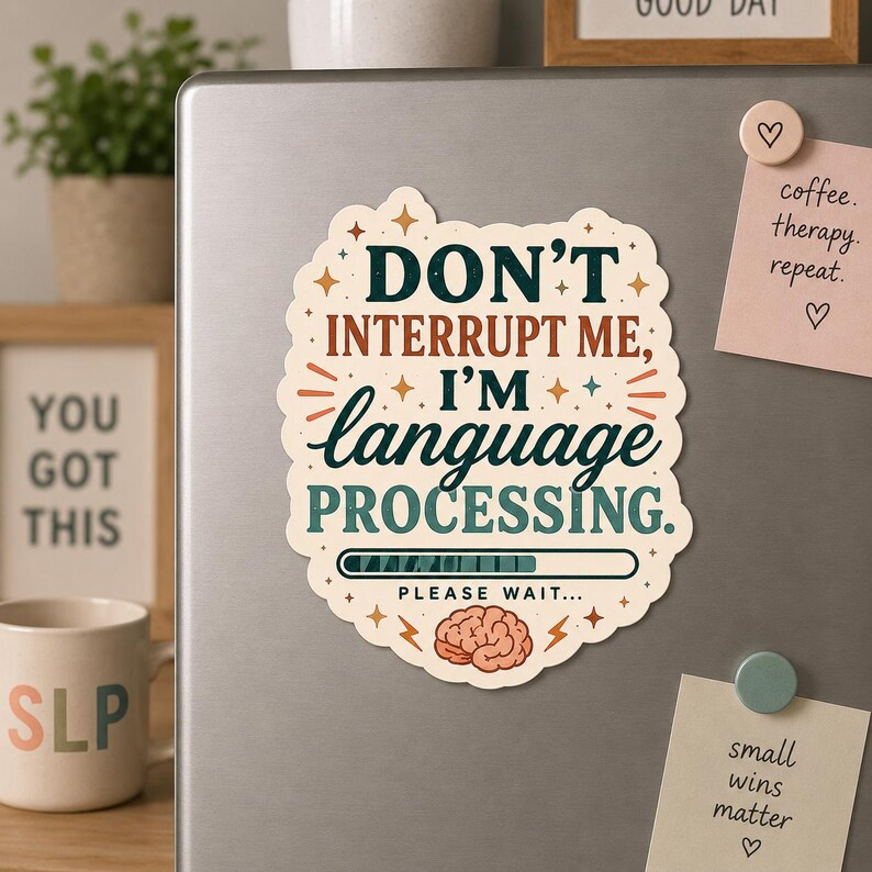 May include: A cream-colored magnet with the text "DON'T INTERRUPT ME, I'M language PROCESSING." The magnet has a brain graphic and a loading bar. The magnet is on a silver refrigerator.