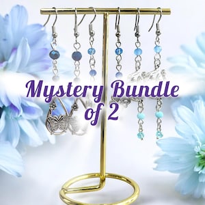 May include: A gold-colored earring display stand holding several pairs of earrings. The earrings feature various blue beads and silver-colored metal accents. The text "Mystery Bundle of 2" is displayed in a purple font.
