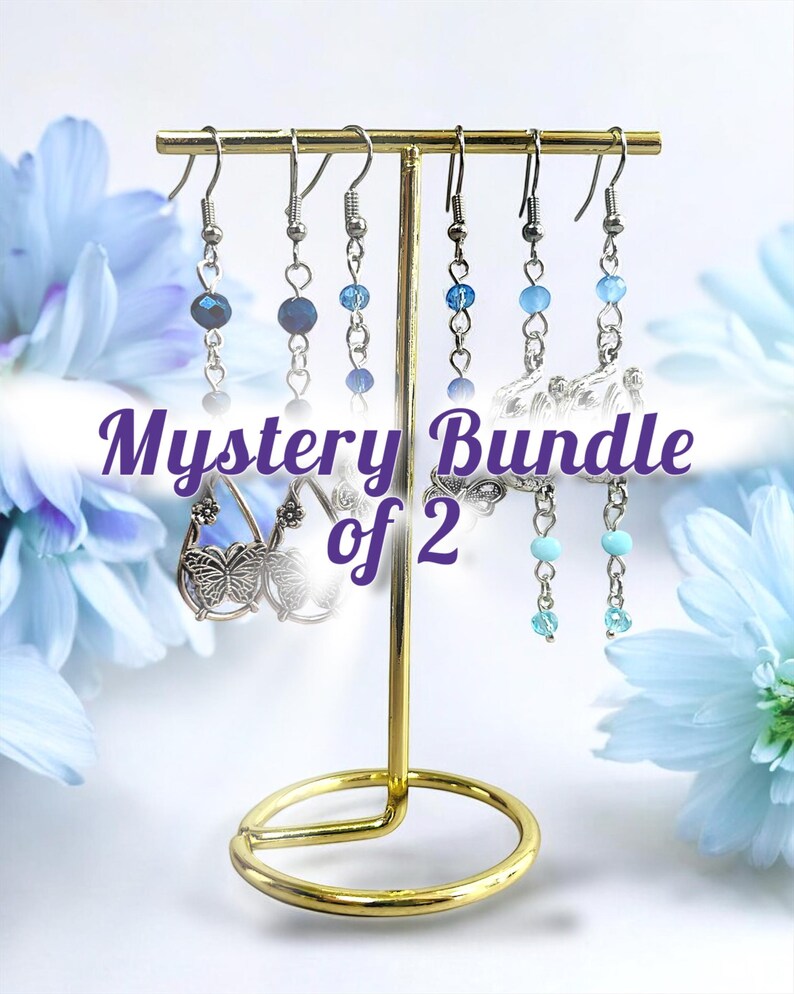 May include: A gold-colored earring display stand holding several pairs of earrings. The earrings feature various blue beads and silver-colored metal accents. The text "Mystery Bundle of 2" is displayed in a purple font.