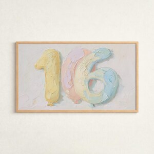 Könnte beinhalten: Gerahmtes Gemälde der Zahl "16", dargestellt als pastellfarbene Luftballons. Die "1" ist gelb, die "6" ist eine Mischung aus Rosa und Blau, und der Hintergrund ist ein helles Off-White. Das Kunstwerk befindet sich in einem hellbraunen Holzrahmen.