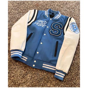May include: A light blue and white varsity jacket with the text "HBCU PRIDE" and a large letter "S". The jacket has white sleeves, black accents, and a patch that says "Spelman College".