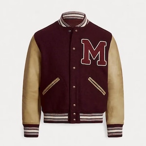May include: Maroon varsity jacket with tan leather sleeves. Features a large white-outlined "M" patch on the chest. The jacket has a striped collar, cuffs, and hem. Includes two front pockets with gold trim and a button-up closure.