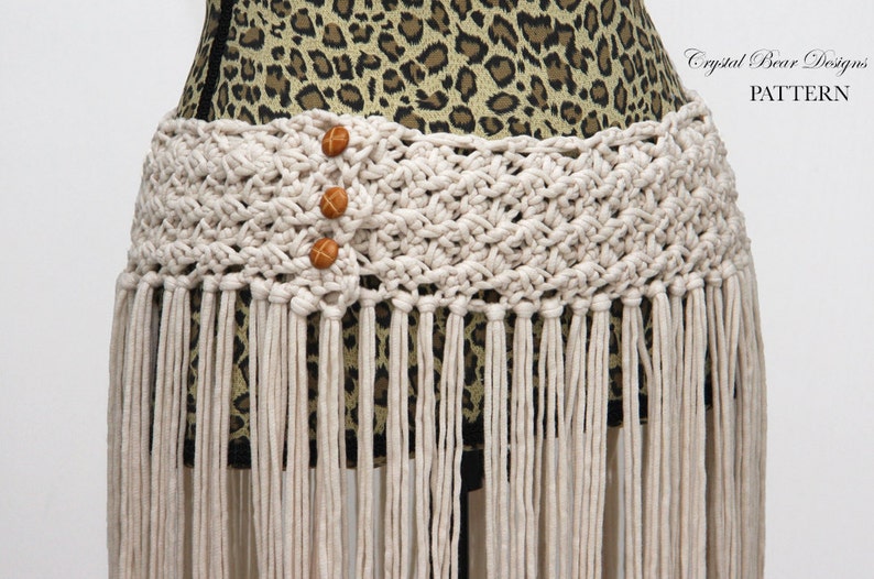 May include: A white crocheted belt with fringe and three brown wooden buttons. The belt is on a leopard print fabric background. Crystal Bear Designs PATTERN.