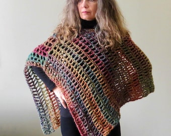 May include: A colorful, open-weave poncho in shades of red, green, yellow, and brown. The poncho has a geometric pattern and is worn over a black top. The garment appears to be handmade, with a textured, knitted or crocheted design.