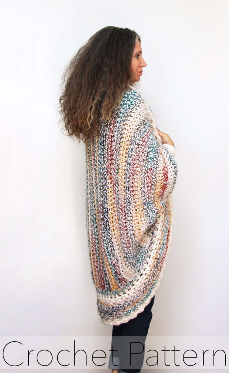 May include: A multi-colored crochet cardigan with a long, flowing design. The cardigan is made with a variety of colors, including white, beige, brown, red, and blue. The cardigan is shown being worn by a person with long, curly hair.
