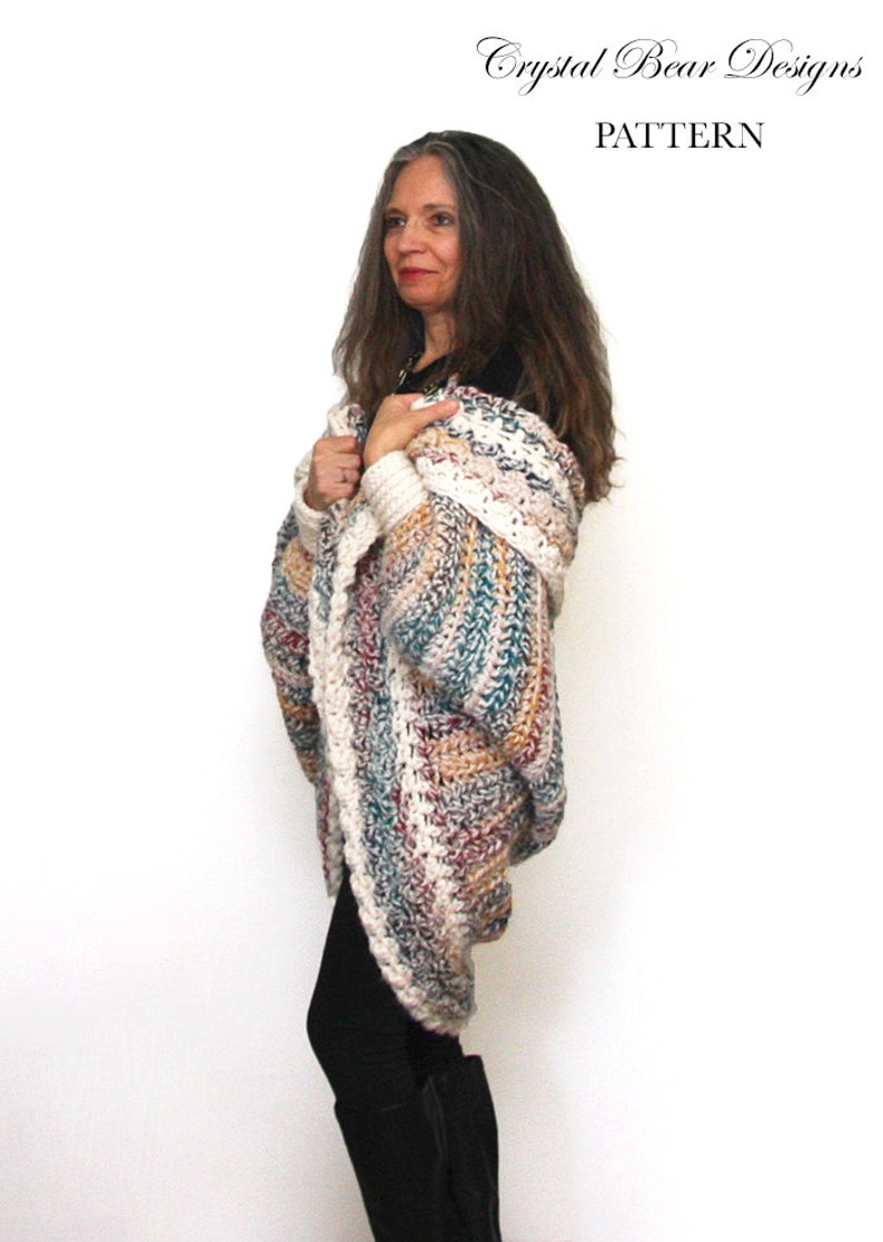 May include: A woman wearing a multi-colored crochet cardigan with a long, flowing design. The cardigan features a variety of colors, including white, brown, teal, and red. The cardigan is draped over her shoulders and arms, and she is wearing black leggings and boots. The text "Crystal Bear Designs PATTERN" is visible at the top of the image.