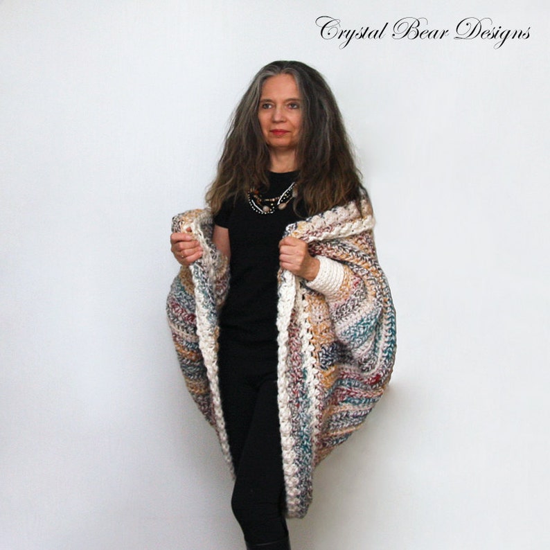 May include: A multi-colored crocheted cardigan with a white trim. The cardigan has a loose fit and is open in the front. The model is wearing the cardigan over a black shirt and black pants.