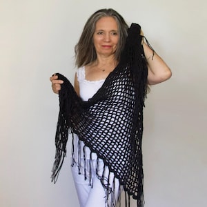 Könnte beinhalten: Ein schwarzer Häkel-Schal mit Fransen. Der Schal ist aus einem leichten, offen gewebten Stoff gefertigt und hat einen zarten, femininen Look.