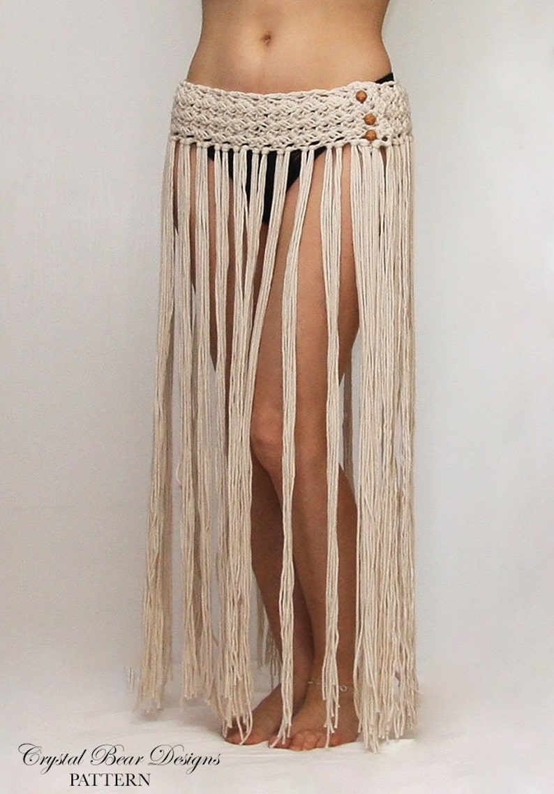 May include: A white crochet skirt with a fringe hem and wooden beads. The skirt is worn by a person with bare legs and feet.