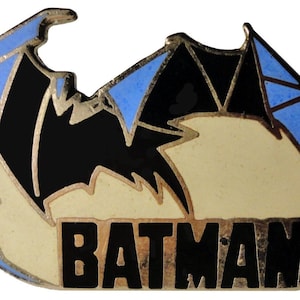 May include: A gold-colored metal pin with a blue and black stylized bat design and the word "BATMAN" in black lettering.