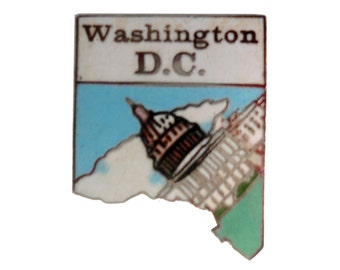 May include: A white enamel pin with a blue and green background. The pin features an illustration of the Capitol Building in Washington D.C. with the text "Washington D.C." at the top.