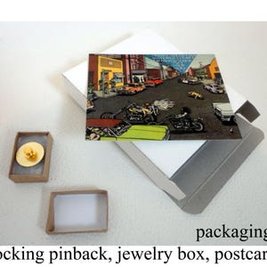 May include: A postcard featuring a vintage illustration of a city street scene with cars and motorcycles. The postcard is packaged in a small cardboard box with a locking pinback.
