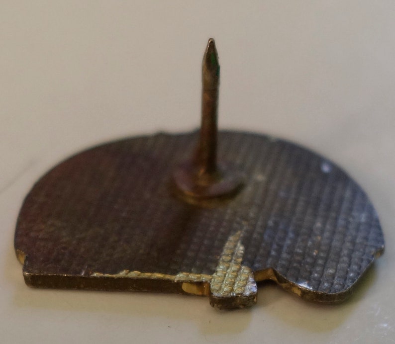 May include: The back of a silver pin with a textured surface and a pointed pin on the back.