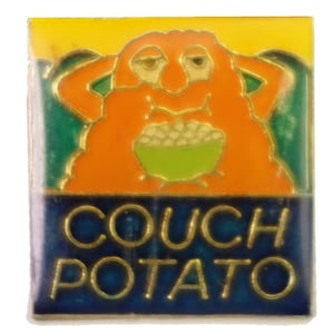 Könnte beinhalten: Eine goldfarbene Anstecknadel mit einer Comicfigur, die auf einem Sofa sitzt und Popcorn isst. Der Text "COUCH POTATO" ist in goldenen Buchstaben auf blauem Hintergrund geschrieben.