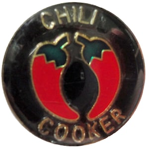 May include: A black and gold round pin with the words "Chili Cooker" and two red chili peppers.