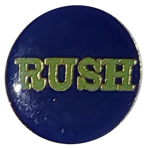 May include: A blue round pin with the word "RUSH" in gold letters with a green outline.