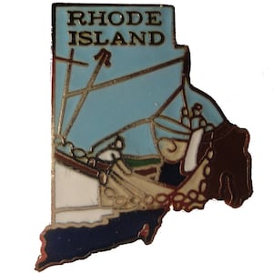 May include: A gold-colored pin shaped like the state of Rhode Island. The pin features a blue and white sailboat with a brown mast and a white background. The words "RHODE ISLAND" are printed in gold on the top of the pin.