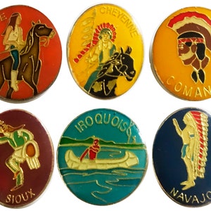 Op de afbeelding: Zes ronde, kleurrijke pinnen met afbeeldingen van indianen en hun stamnamen. De stammen zijn Apache, Cheyenne, Comanche, Sioux, Iroquois en Navajo.