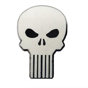 May include: A white skull with black eye sockets and a black outline. The skull has a black line down the center of the nose and seven black lines across the bottom of the skull.