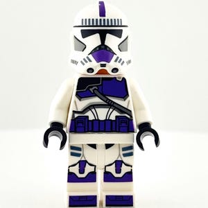May include: A Lego clone trooper minifigure in white and purple. The figure has a white helmet with purple stripes and black details. The armour is white with purple and black accents. The figure has black hands and is standing upright.