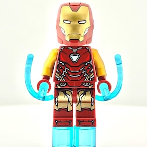 Puede incluir: Una figura de Lego de Iron Man con un casco y armadura rojos y dorados. La figura tiene brazos amarillos, piernas rojas y pies azules translúcidos. Efectos de energía azules se extienden de las manos.
