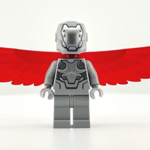 May include: A gray Lego minifigure with a silver helmet and chest armor, and red wings. The figure has a detailed design and is standing against a white background. The wings are a vibrant red color.