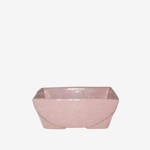 May include: A pink ceramic planter with a square top and curved sides. The planter has a speckled texture and a glossy finish. The base has a ribbed design. This decorative planter is suitable for small plants or succulents.