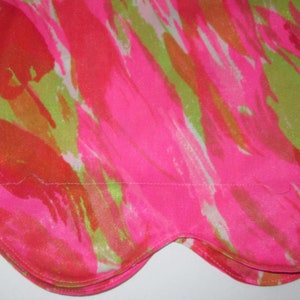 K&ouml;nnte beinhalten: Nahaufnahme eines Stoffes mit einem lebendigen, abstrakten Design. Das Muster zeigt kr&auml;ftige Striche in Pink, Orange und Limettengr&uuml;n, die ein dynamisches und farbenfrohes Bild erzeugen. Der Stoff hat einen gewellten Rand.