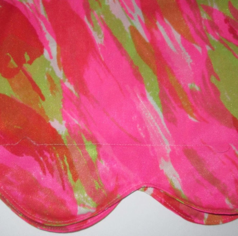 K&ouml;nnte beinhalten: Nahaufnahme eines Stoffes mit einem lebendigen, abstrakten Design. Das Muster zeigt kr&auml;ftige Striche in Pink, Orange und Limettengr&uuml;n, die ein dynamisches und farbenfrohes Bild erzeugen. Der Stoff hat einen gewellten Rand.
