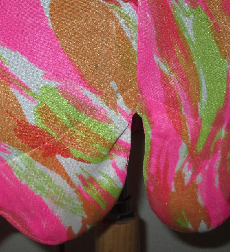 K&ouml;nnte beinhalten: Nahaufnahme eines Stoffes mit lebendigem, abstraktem Muster. Das Design zeigt kr&auml;ftige Striche in Neonrosa, Orange, Gr&uuml;n und Wei&szlig;. Der Stoff ist wahrscheinlich ein Kleidungsst&uuml;ck, mit einem Schlitz am Saum.