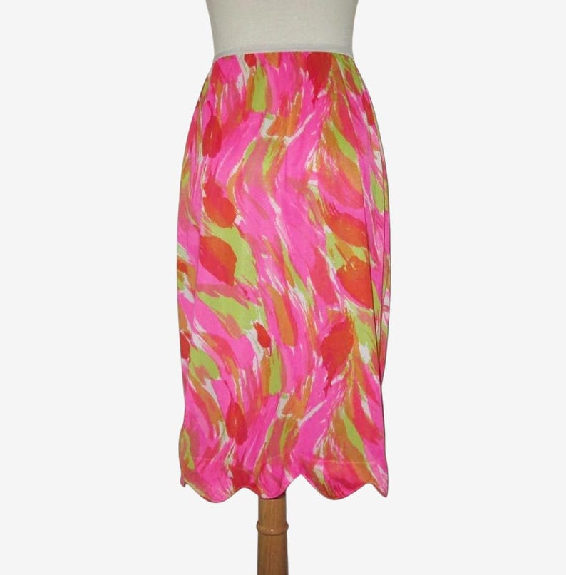 K&ouml;nnte beinhalten: Ein lebendiger, knielanger Rock mit einem farbenfrohen, abstrakten Muster. Das Design zeigt kr&auml;ftige Striche in Pink, Gr&uuml;n und Orange, die einen dynamischen Look erzeugen. Der Rock hat einen wellenf&ouml;rmigen Saum, der dem Design eine elegante Note verleiht. Der Rock ist ca. 76 cm lang.
