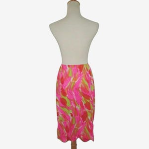 K&ouml;nnte beinhalten: Ein lebendiger, knielanger Rock mit einem farbenfrohen, abstrakten Muster. Der Rock hat eine hohe Taille und einen gewellten Saum. Das Design umfasst rosa, gr&uuml;ne und orangefarbene Striche auf wei&szlig;em Hintergrund. Der Rock wird auf einer Schaufensterpuppe pr&auml;sentiert.
