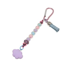 May include: A keychain with a pink carabiner clip, a strand of iridescent beads, and a light blue tassel. The keychain also features a lavender cloud charm and a pink and black beaded accent.