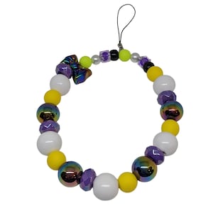 Könnte beinhalten: Ein Telefonanhänger mit bunten Perlen. Der Anhänger hat weiße, gelbe, violette und irisierende Perlen sowie eine kleine schleifenförmige Perle. Eine schwarze Schnur ist zur einfachen Befestigung an einem Telefon oder anderen Gerät angebracht.