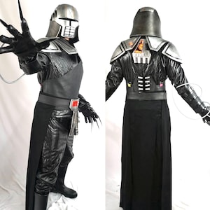 Pode incluir: Um traje preto e prateado com um capacete, armadura de ombro e luvas com garras longas. O traje inclui uma saia longa preta, um cinto com um detalhe vermelho e botas pretas. Fios se estendem das luvas.