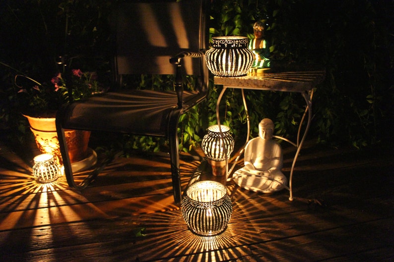 May include: A patio setting with a chair, a table, and several decorative lanterns. The lanterns are made of metal and have a geometric design. The lanterns are lit and casting a warm glow on the surrounding area.